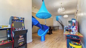 A room with a blue slide, arcade games, a chandelier, and a staircase. - McKinley Mansion Half Building, sleeps 35, Gym, Arcade Room (Pocatello)