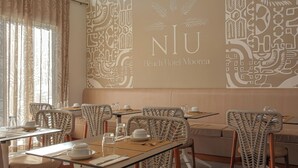 A restaurant with wicker chairs, tables set with plates, glasses, and cutlery. The wall features a large logo and decorative patterns. - Niu Beach Hotel Moorea (Moorea-Maiao)