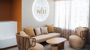 A modern lounge area with a sofa, two armchairs, and a coffee table. A circular logo with the text "NJU Beach Hotel Noorco" is displayed on the wall. - Niu Beach Hotel Moorea (Moorea-Maiao)