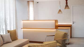 A modern hotel room with a sofa, a chair, a desk, and pendant lighting.