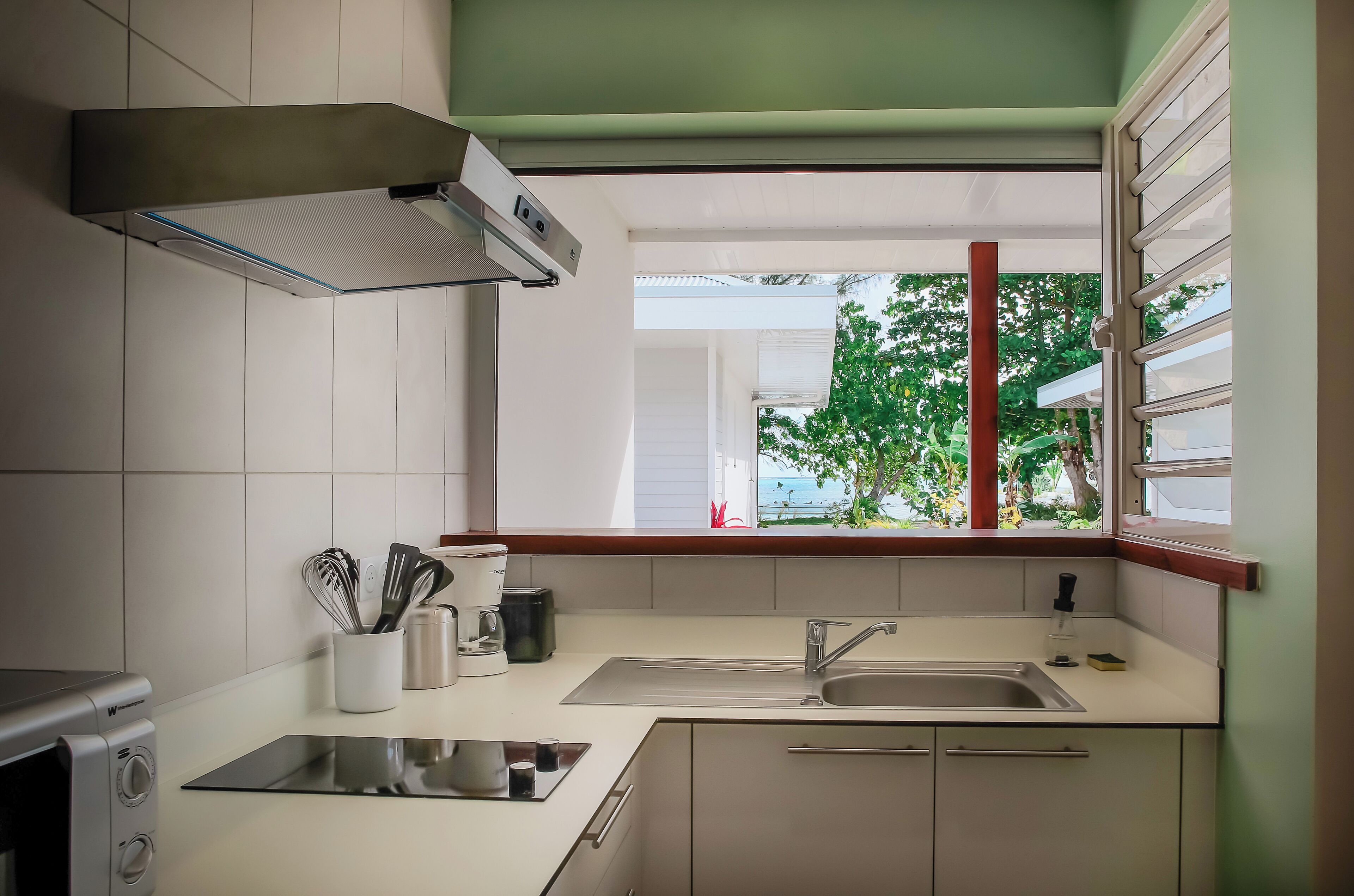 A modern kitchen with a built-in stove, a sink, and a window with a view of greenery.