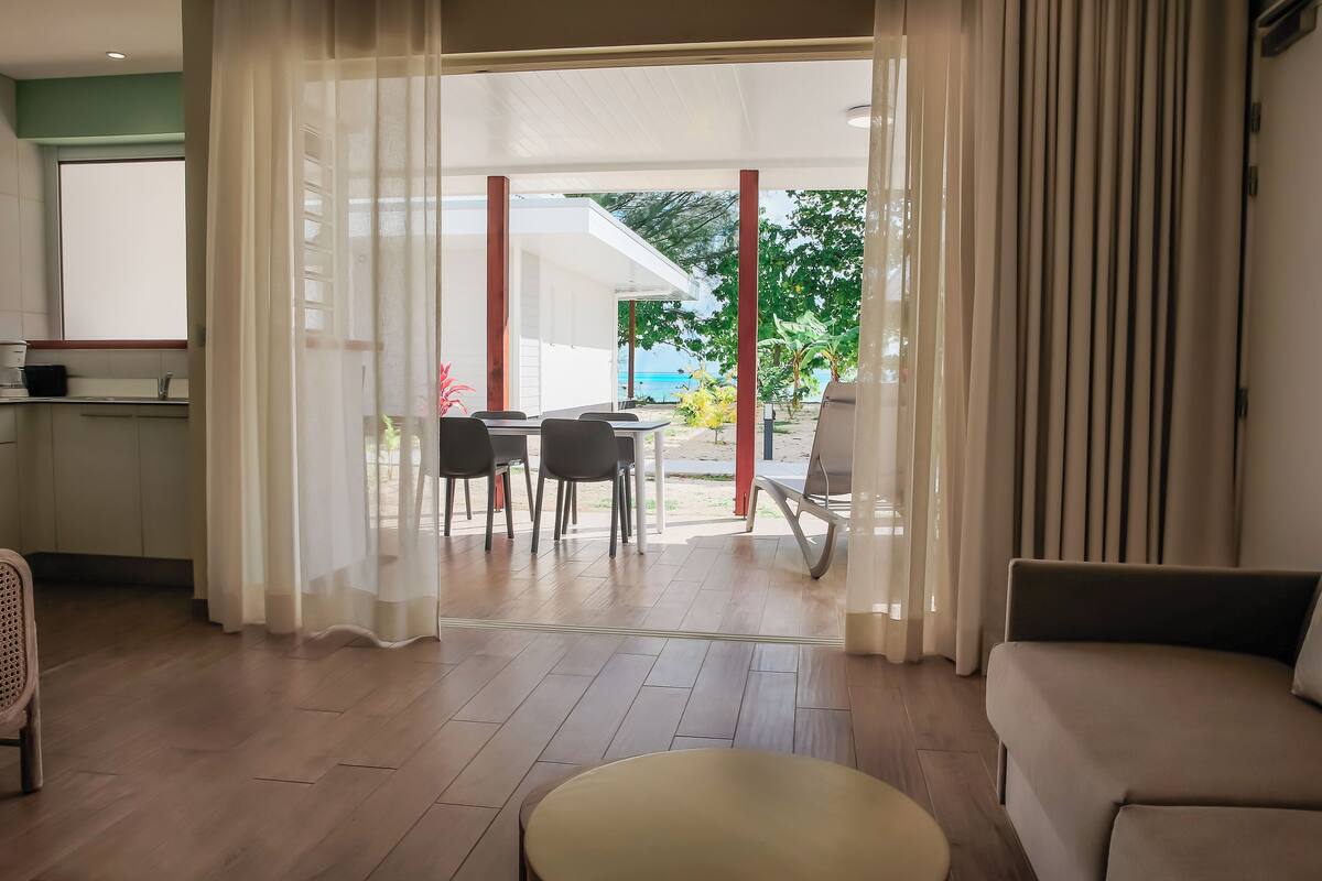 A modern living room with a sofa, a dining table with chairs, and a view of the outdoors.