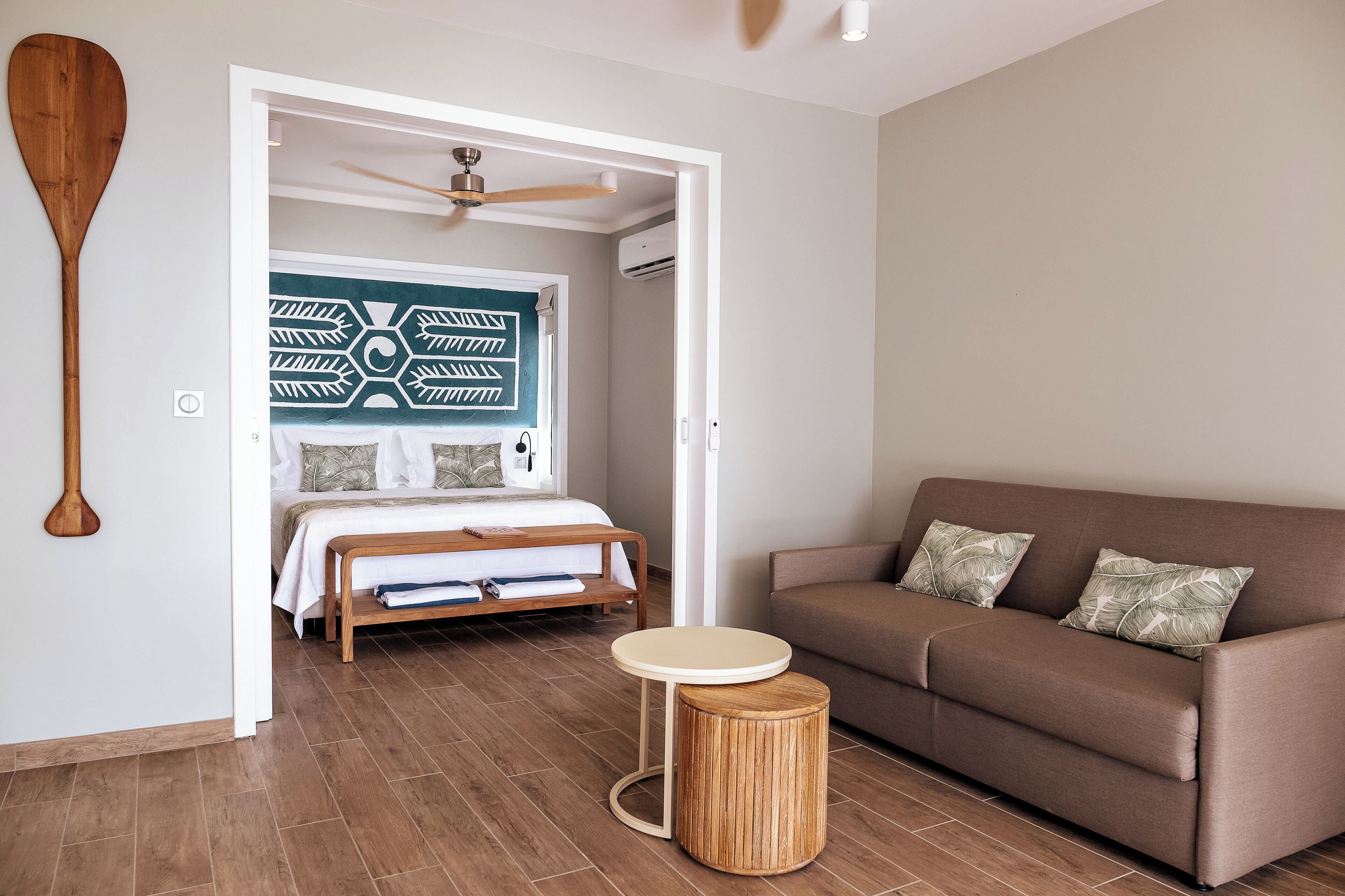 A bedroom with a bed, a brown sofa, a round wooden table, and a ceiling fan.