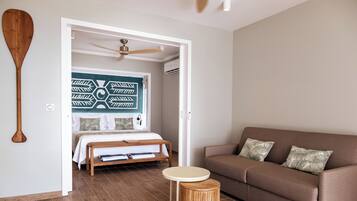 A bedroom with a bed, a brown sofa, a round wooden table, and a ceiling fan.