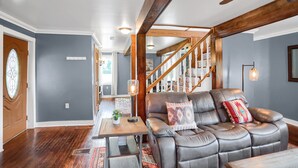 Ein Wohnzimmer mit Ledersofa, Holzbalken, einer Treppe und Blick ins Freie.