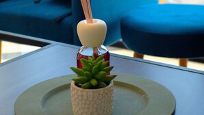 A small potted succulent on a green plate on a table, with a blue chair and a view of a cityscape in the background.