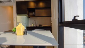 A modern kitchen with dark cabinets, a white refrigerator, and a microwave. There's a dining table with a vase and a small plant on it.