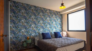 A bedroom with a floral wallpaper, a bed with a brown quilt, and a window with a view.