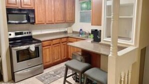 A kitchen with wooden cabinets, a microwave, a stove, and a small bar area. - Unique Family home (St. Louis)