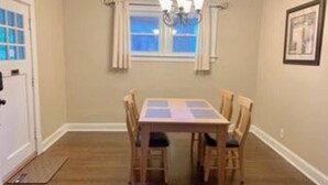 A dining room with a rectangular table, four chairs, a chandelier, a window with curtains, and a framed picture on the wall. - Unique Family home (St. Louis)