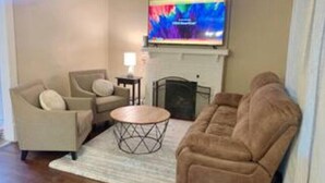 A living room with a beige sofa, a brown sofa, a coffee table, and a flat-screen TV mounted above a fireplace. - Unique Family home (St. Louis)