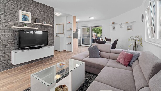 Una sala de estar moderna con una pared de piedra, un televisor de pantalla plana, una mesa de centro de vidrio y un sofá gris.