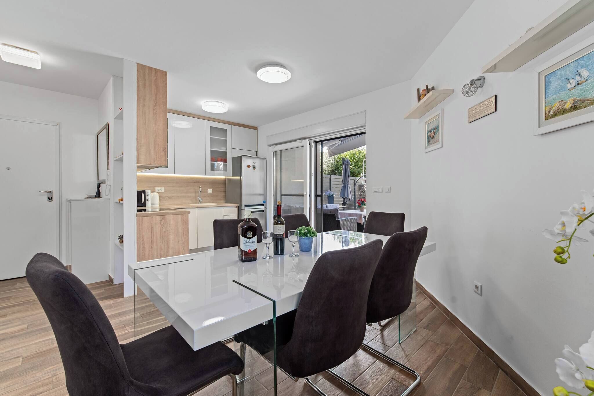 Una cocina moderna con armarios blancos, encimera de madera y mesa de comedor de vidrio con cuatro sillas.
