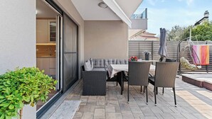 Un patio al aire libre con mesa y sillas, un área de estar con cojines y una pequeña planta en maceta.