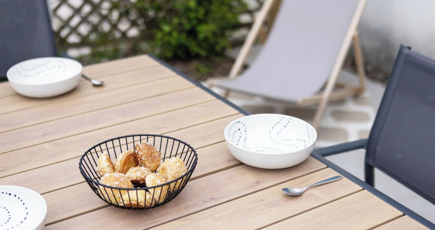 Une table en bois sur laquelle se trouvent un bol en métal rempli de biscuits, un bol blanc orné de motifs à pois et une cuillère.