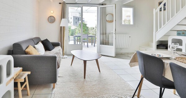 A modern living room with a grey sofa, a round coffee table, and a dining area with a table and chairs. - Maison paisible avec jardin et piscine – Esprit vacances (Les Sables-d´Olonne)