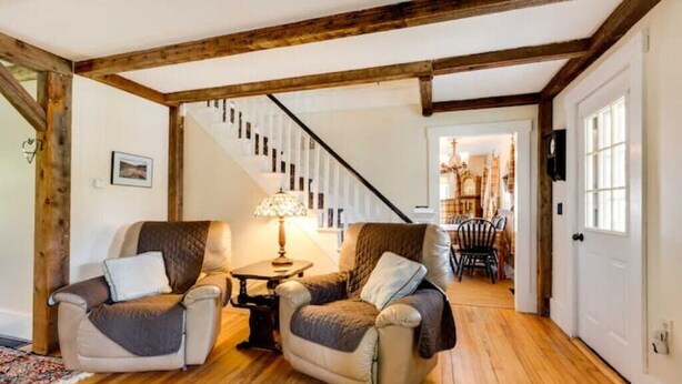 Un salón acogedor con dos sillones, una escalera de madera y un comedor al fondo.