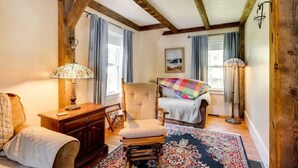 Una habitación acogedora con techo de madera, una cama con manta de colores, una silla, una lámpara y una alfombra.
