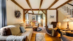 Un salón acogedor con techo de madera, un sofá, un sillón y una mesa con una lámpara.