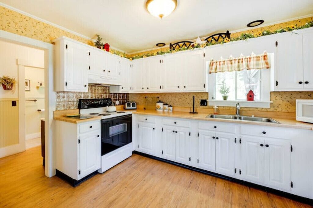 A kitchen with white cabinets, a stove, a microwave, and a sink.