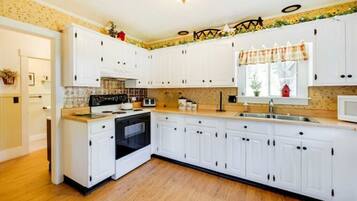 A kitchen with white cabinets, a stove, a microwave, and a sink.
