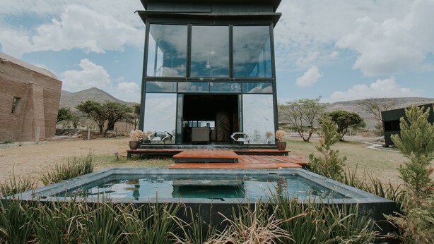 A modern house with a glass facade, a pool, and a patio area. - K NAJ Community (San Miguel de Allende)