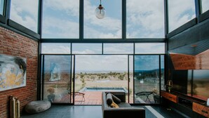 A modern interior with large windows, a brick wall, and a view of a desert landscape. - K NAJ Community (San Miguel de Allende)
