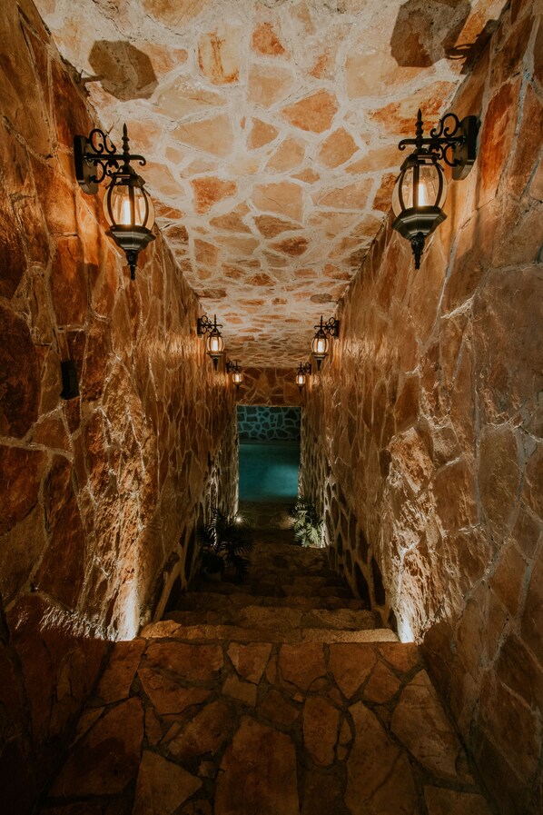 A stone-walled corridor with a stone floor, leading to a room with a blue-tiled wall.
