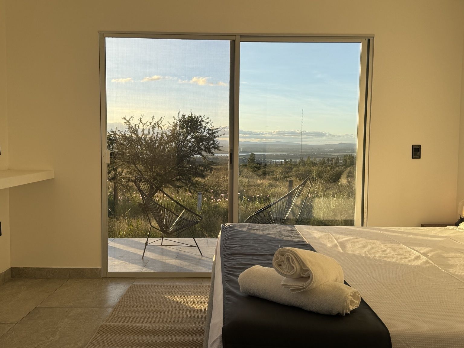Une chambre d’hôtel avec un lit, une grande fenêtre donnant sur la campagne et une chaise à l’extérieur.