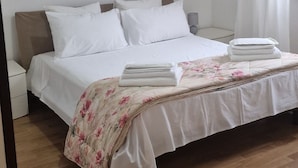A neatly made bed with white linens, a floral-patterned blanket, and a modern pendant light above it.