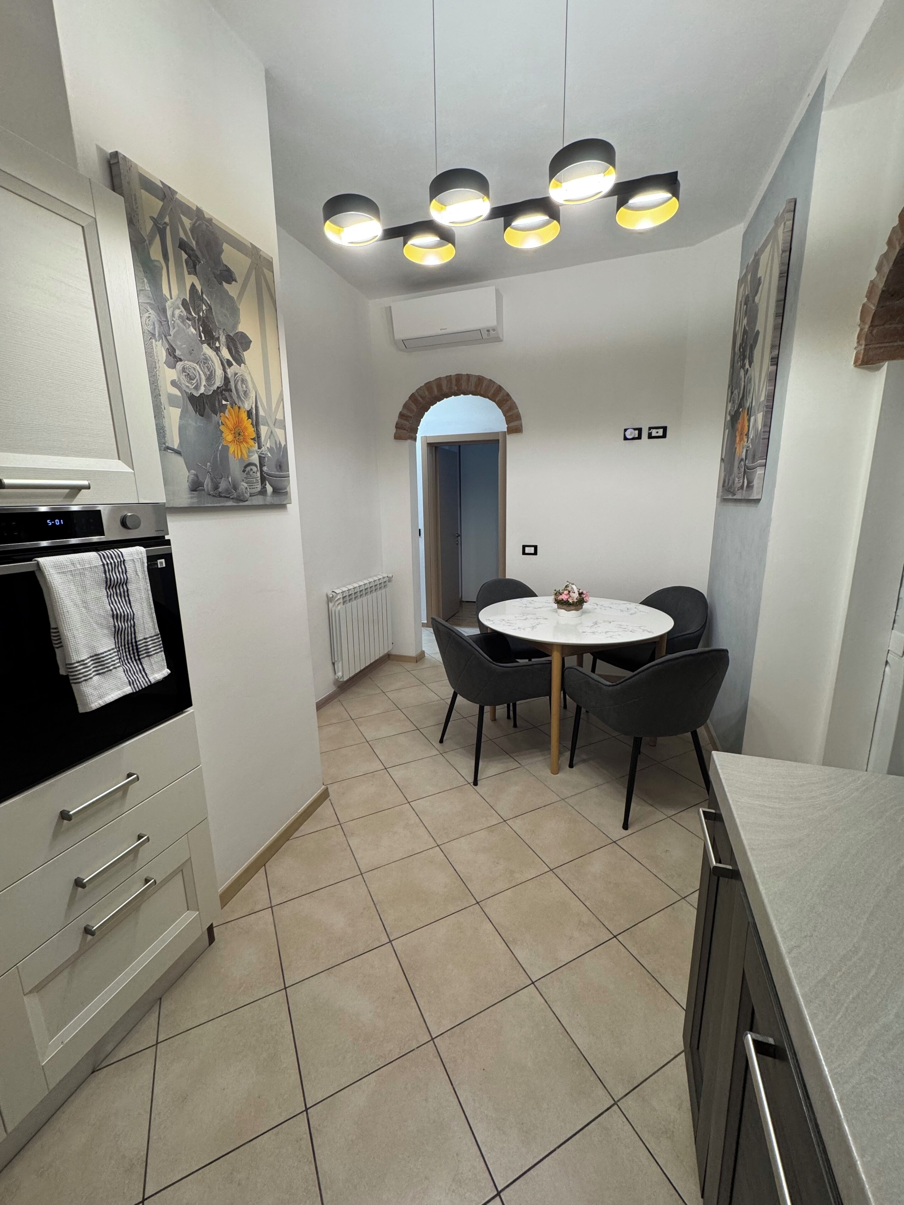 A modern kitchen with a dining area, featuring a tiled floor, a built-in oven, a wall-mounted air conditioner, and a ceiling light fixture.