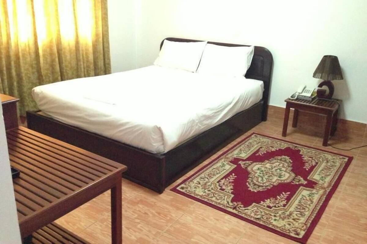 Ein Hotelzimmer mit einem Bett, einem Nachttisch mit Lampe, einem Telefon und einem dekorativen Teppich.