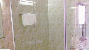 Une douche fermée par des parois de verre, avec un sol carrelé, un lavabo blanc et un porte-serviettes.