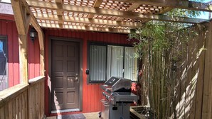 A wooden deck leading to a red building with a door and a window. A barbecue grill is positioned on the deck. - Shangrila Luxury Waterfront Panorama Suite | Oceanfront Seating & Beach Access (Pender Island)