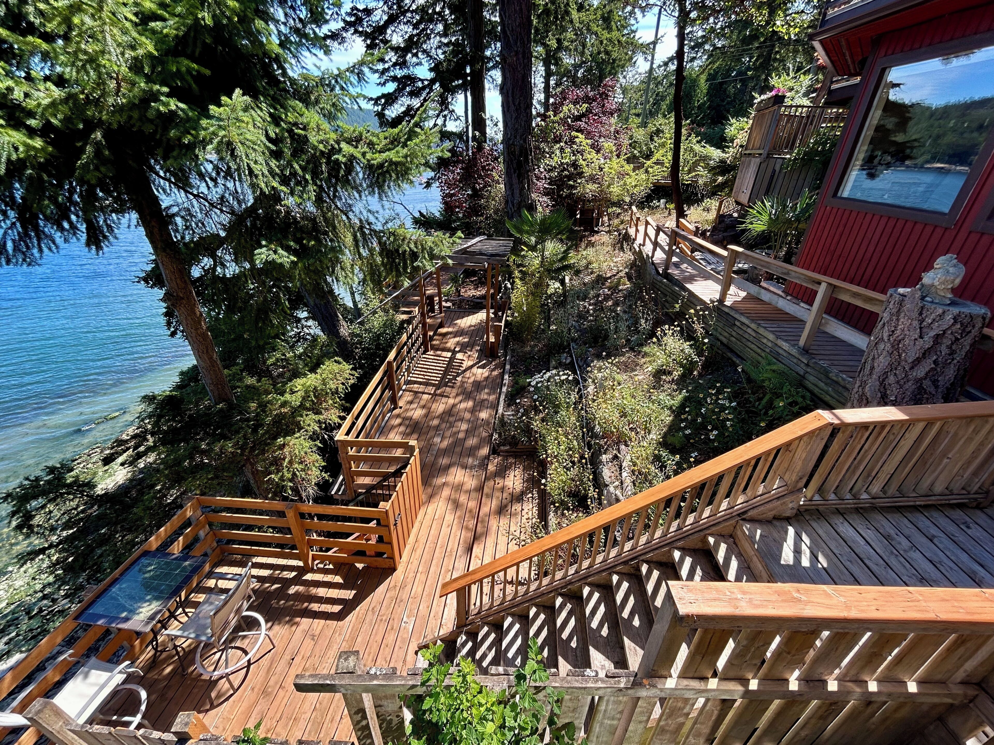 A wooden deck with a table and chairs, overlooking a body of water and surrounded by trees.