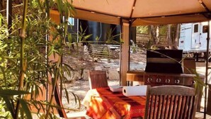 Un patio al aire libre con una parrilla, sillas de madera y una mesa cubierta con mantel rojo.