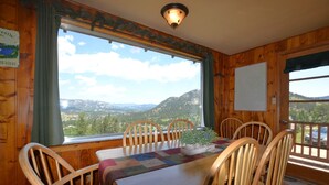 Une salle à manger en bois avec une table et des chaises, une vue sur les montagnes et un tableau blanc accroché au mur.