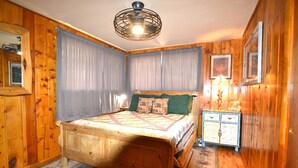 Une chambre à coucher aux murs lambrissés, avec un lit en bois, une table de chevet, une lampe et un tableau encadré accroché au mur.