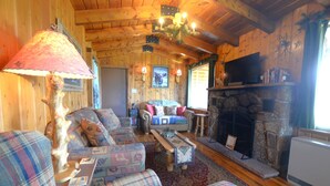 L’intérieur d’un chalet confortable, avec des meubles à carreaux, une cheminée en pierre et un téléviseur fixé au mur.