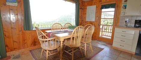 A wooden interior with a dining table and chairs, a kitchen area, and a view of mountains through large windows.