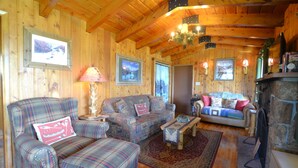 L’intérieur d’un chalet confortable, avec des murs en rondins, un canapé à motifs écossais, une cheminée et des tableaux encadrés.