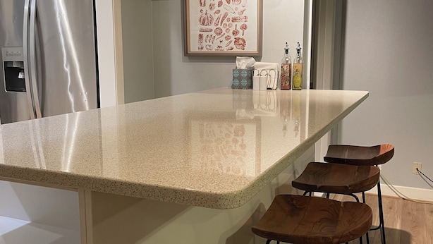 A kitchen with a granite countertop, stainless steel refrigerator, wooden bar stools, and a framed picture on the wall. - An elegant and comfy Beaverton Home (Beaverton)