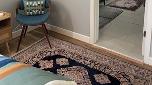 A room with a blue armchair, a patterned rug, and artwork on the walls. - An elegant and comfy Beaverton Home (Beaverton)
