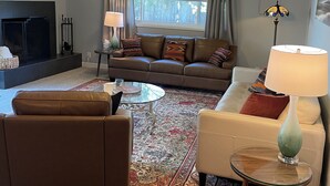 A living room with a sofa, armchairs, a coffee table, a fireplace, and a large window with curtains. - An elegant and comfy Beaverton Home (Beaverton)