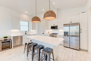 A modern kitchen with white cabinetry, stainless steel appliances, and a large island with bar stools. - Modern Luxury Villa in Prime Port A - Private Pool, Golf Cart, Ocean Views! (Port Aransas)