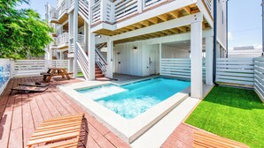 En bygning med flere etager, en swimmingpool, træterrasse og et lille græsstykke.
