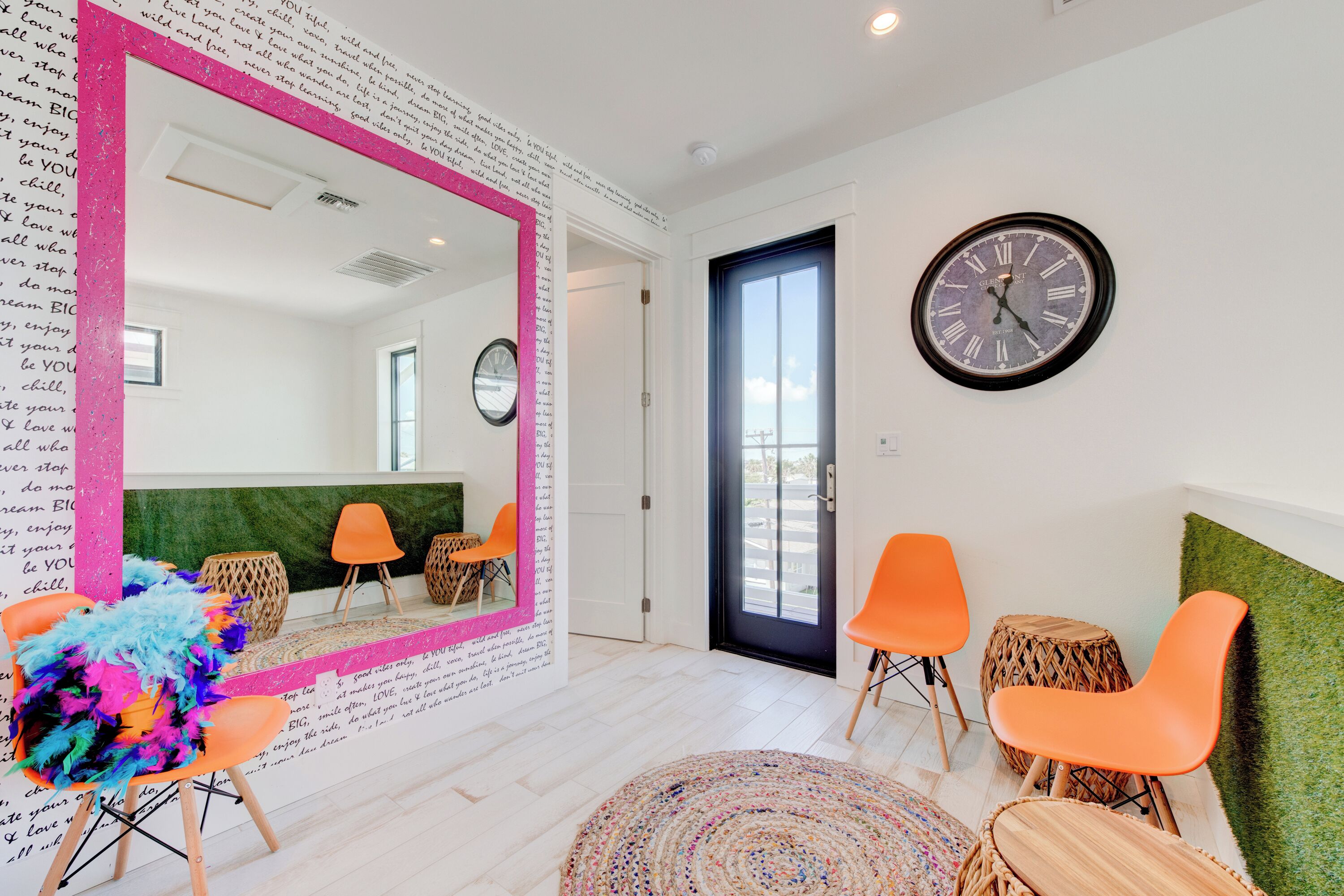 A modern room with a large mirror, orange chairs, a round table, and a clock on the wall.