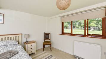A bedroom with a bed, bedside table, chair, window, radiator, and a hanging light fixture.