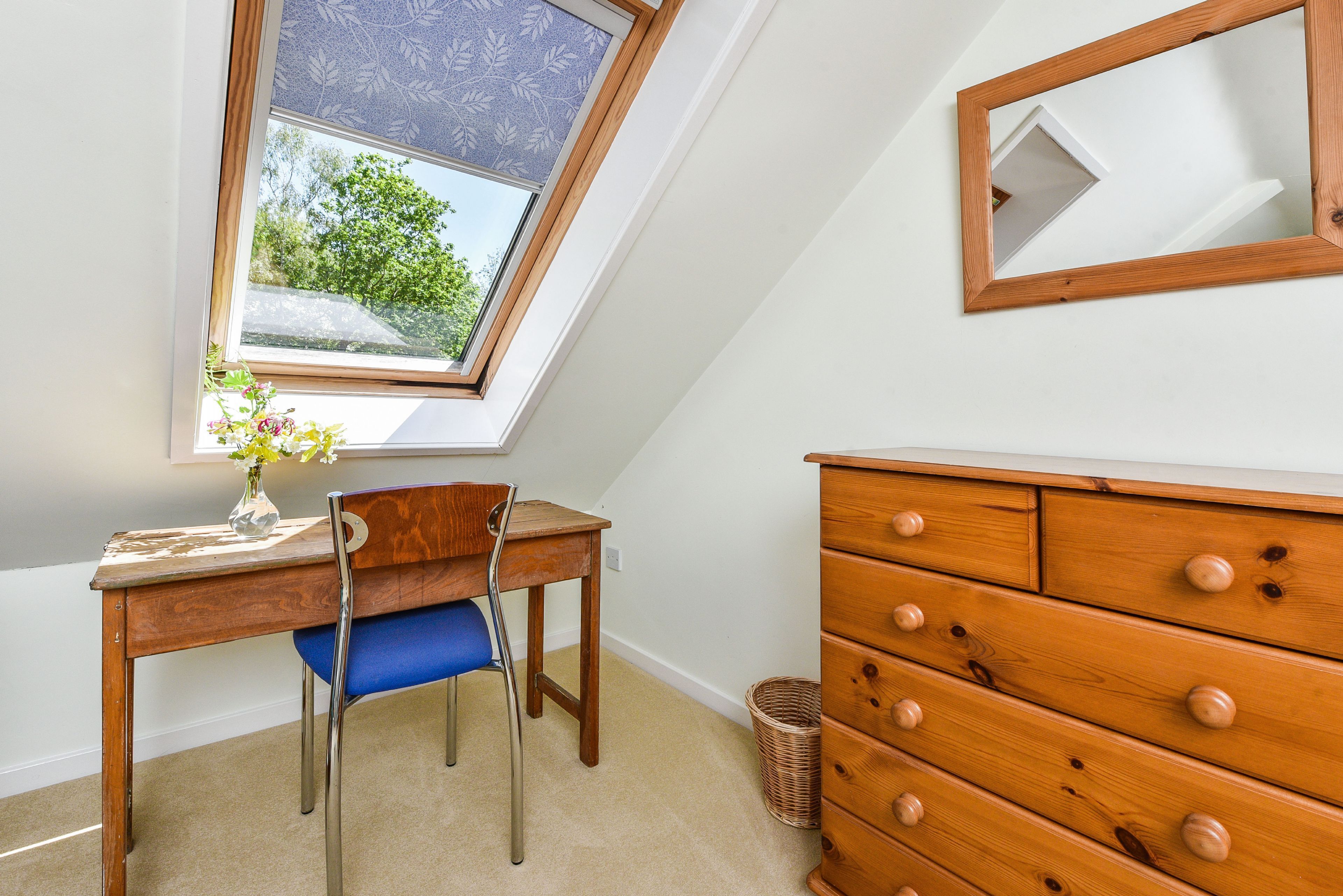 A room with a wooden desk, a chair, a dresser, and a window with a view of greenery.