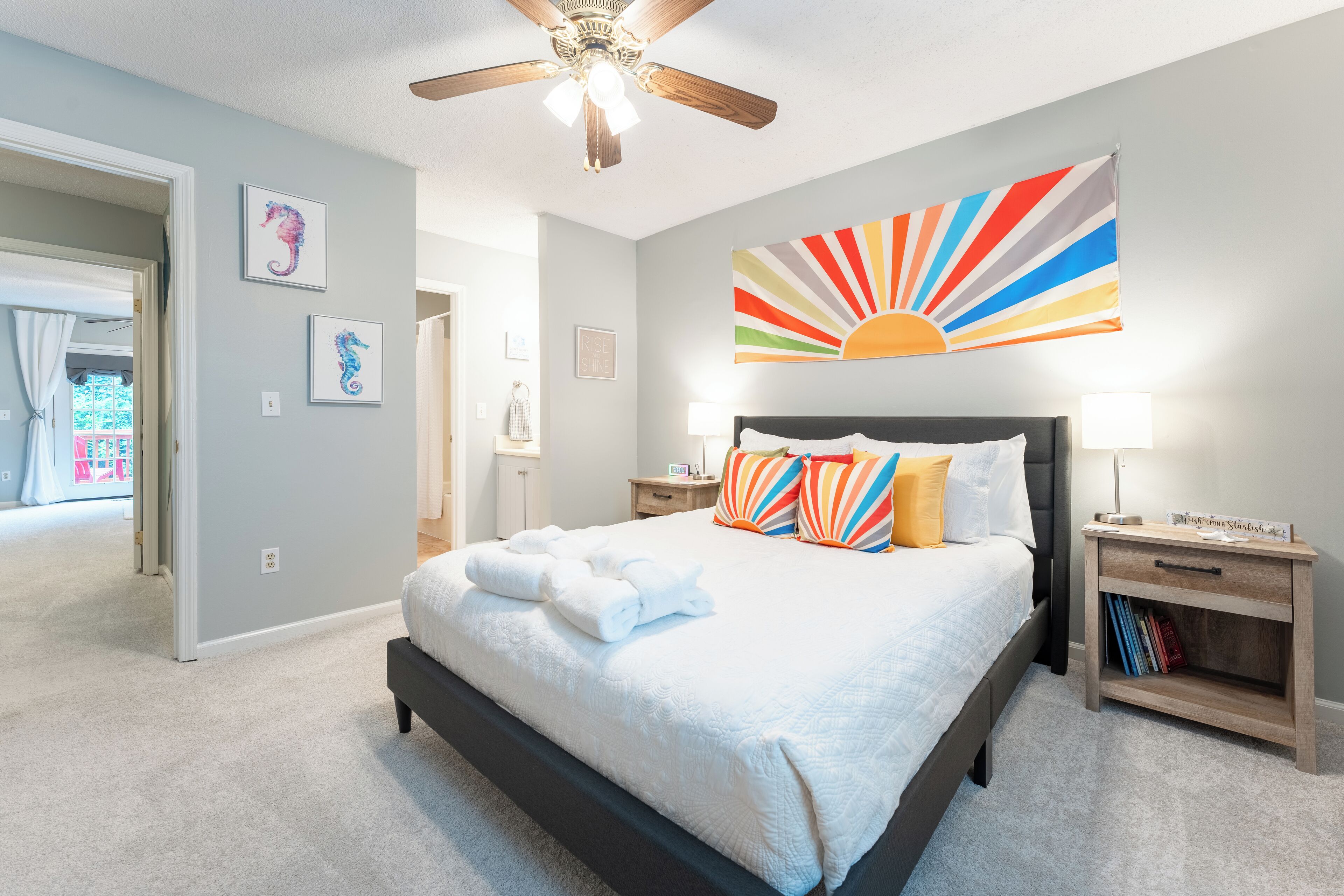 A bedroom with a bed, a nightstand, a ceiling fan, and a wall with a sunburst artwork.